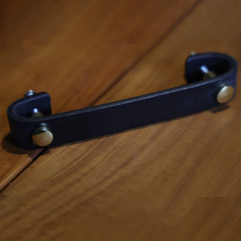 Brown leather drawer pulls with brass accents on a wooden surface. Rustic cabinet handles.